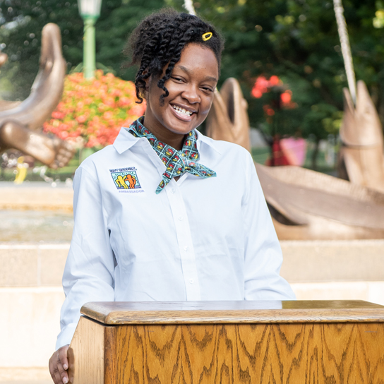 A female Buddy Ambassador standing at a podium delivering a speech