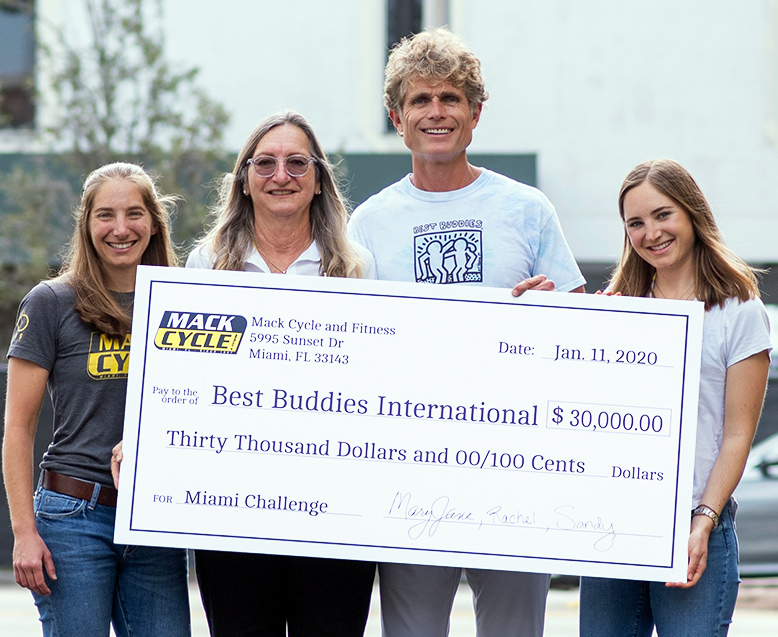 Anthony Shriver, Founder of Best Buddies International, holds a large presentation check for $30,000 dollars. The owner and her two daughters are standing next to him.