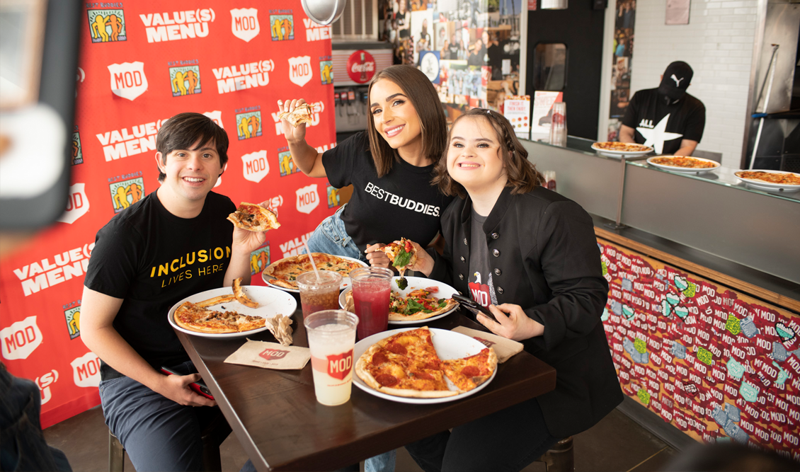 Best Buddies Supporter, Olivia Cumpo, one female and one male Best Buddies participants, are eating pizza at MOD's Pizza.