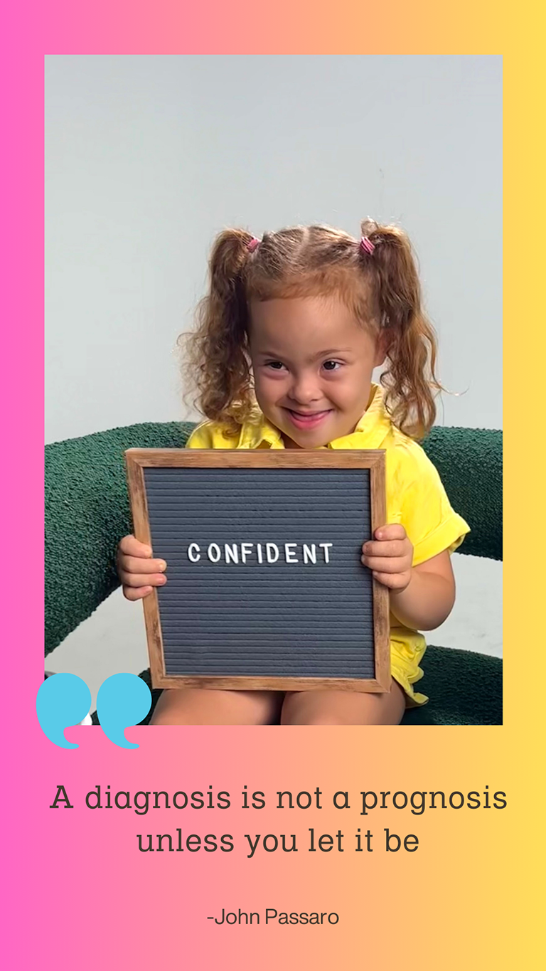  A young girl with down syndrome is smiling and holding a sign that says, 